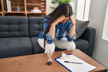 Young beautiful hispanic woman patient stressed sitting on sofa at psychology clinic