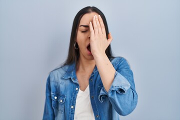 Hispanic woman standing over blue background yawning tired covering half face, eye and mouth with hand. face hurts in pain.