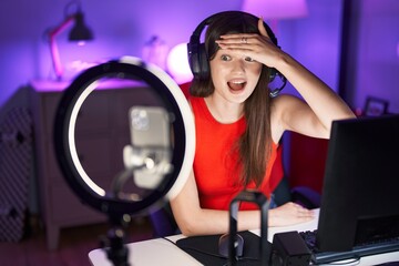 Fototapeta na wymiar Young caucasian woman playing video games recording with smartphone stressed and frustrated with hand on head, surprised and angry face