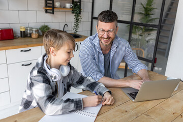 Father helping his teenage son with homework while working from home in the kitchen. Concept of...