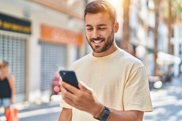 Young hispanic man smiling confident using smartphone at street