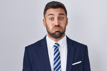 Handsome hispanic man wearing suit and tie puffing cheeks with funny face. mouth inflated with air, crazy expression. - obrazy, fototapety, plakaty