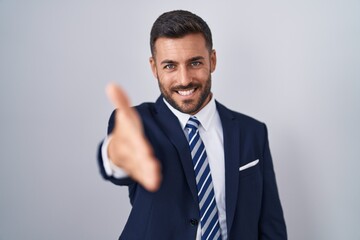 Handsome hispanic man wearing suit and tie smiling friendly offering handshake as greeting and welcoming. successful business.