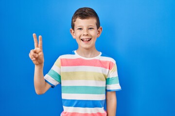 Young caucasian kid standing over blue background showing and pointing up with fingers number two while smiling confident and happy.