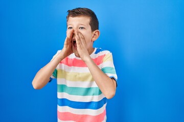 Young caucasian kid standing over blue background shouting angry out loud with hands over mouth