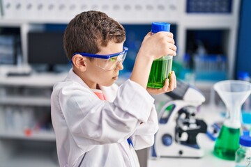 Blond child wearing scientist uniform holding bottle at laboratory