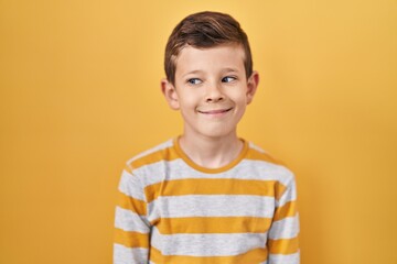 Young caucasian kid standing over yellow background smiling looking to the side and staring away thinking.