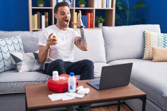 Young Hispanic Man Watching Video On Laptop On How To Use First Aid Kit Celebrating Victory With Happy Smile And Winner Expression With Raised Hands