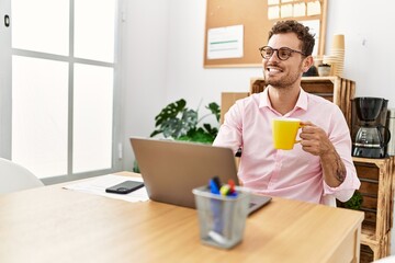 Young hispanic man drinking coffee working at office