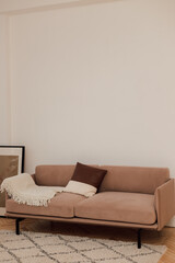 A beige sofa stands near a white wall next to a green flower