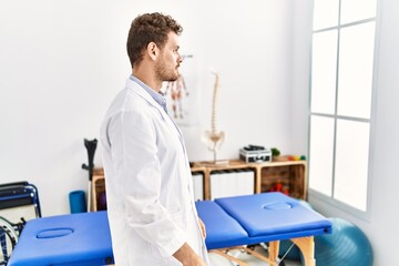 Obraz premium Handsome young man working at pain recovery clinic looking to side, relax profile pose with natural face with confident smile.