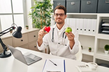 Young hispanic man working at dietitian clinic relaxed with serious expression on face. simple and...