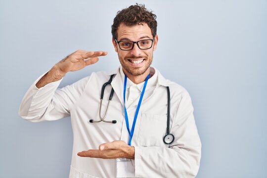 Young hispanic man wearing doctor uniform and stethoscope gesturing with hands showing big and large size sign, measure symbol. smiling looking at the camera. measuring concept.