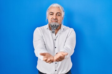 Middle age man with grey hair standing over blue background smiling with hands palms together receiving or giving gesture. hold and protection