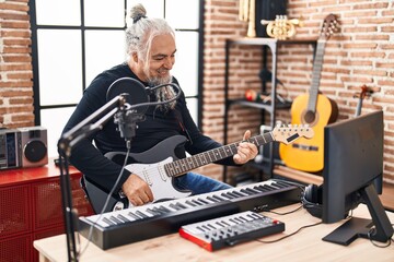 Middle age grey-haired man musician singing song playing electrical guitar at music studio