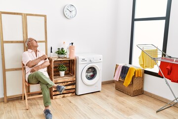 Senior man waiting for washing machine sitting on chair at laundry room