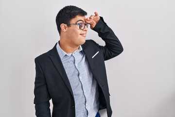 Young hispanic man with down syndrome wearing business style very happy and smiling looking far away with hand over head. searching concept.