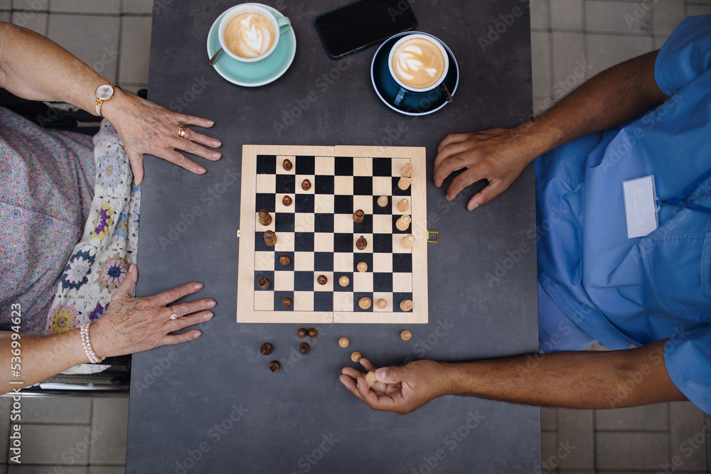 Poster Top view of caregiver playing chess and drinking coffe with his client outdoor at cafe.