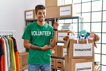 Young handsome hispanic man wearing volunteer t shirt at donations stand smiling with happy face...