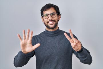 Naklejka premium Handsome latin man standing over isolated background showing and pointing up with fingers number seven while smiling confident and happy.