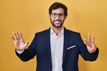 Handsome latin man standing over yellow background showing and pointing up with fingers number eight while smiling confident and happy.