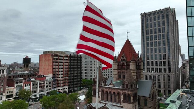 American USA and Massachusetts flags wave on windy day. Boston Trinity Church in background. Aerial establishing shot of top tourist attractions in Boston MA.