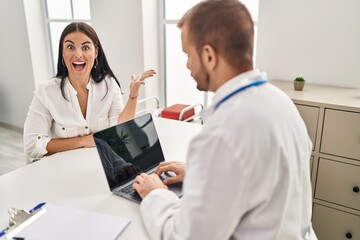 Fototapeta premium Young hispanic woman at the doctor celebrating victory with happy smile and winner expression with raised hands