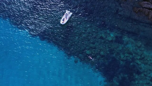 Aerial Birds Eye View Of Boats Moored Of Cala Coticcio Coastline In Clear Blue Waters With Person Swimming Below. Rising Shot