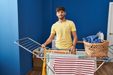 Young arab man smiling confident hanging clothes on clothesline at laundry room