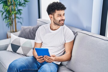 Young arab man using touchpad sitting on sofa at home