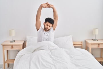 Young arab man waking up stretching arms at bedroom