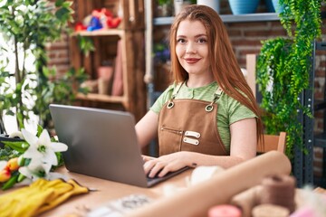 Young redhead woman florist smiling confident using laptop at flower shop