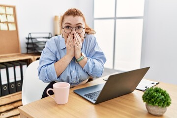 Young redhead woman working at the office using computer laptop laughing and embarrassed giggle...