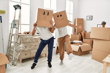 Two hispanic men couple playing with funny cardboard boxes on head at new home