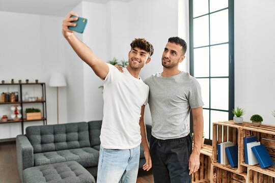 Two hispanic men couple making selfie by the smartphone hugging each other at home