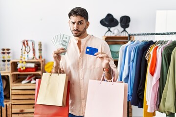 Young hispanic man holding shopping bags and credit card skeptic and nervous, frowning upset because of problem. negative person.