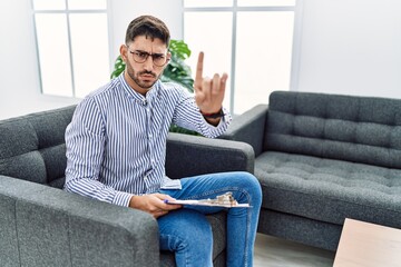 Young psychologist man at consultation office pointing with finger up and angry expression, showing...