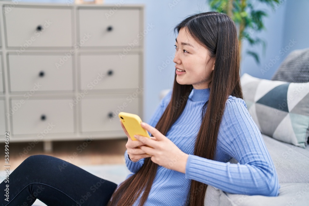 Sticker Chinese woman using smartphone sitting on floor at home