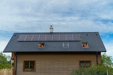 Happy family waving from skylight windows in their new house with solar panels on the roof....