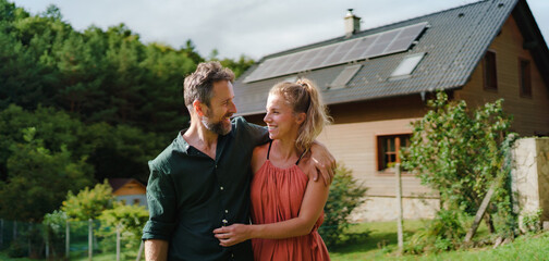 Happy couple standying near their house with solar panels. Alternative energy, saving resources and...