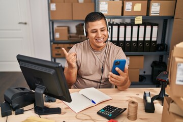 Hispanic young man working at small business ecommerce on video call smiling happy pointing with hand and finger to the side
