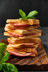 big sandwich with ham and cheese on a board on a black background