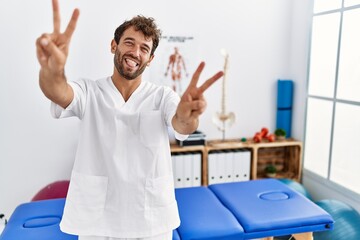 Young handsome physiotherapist man working at pain recovery clinic smiling with tongue out showing...