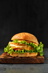 burger with meat, cheese and salad on a board on a black background