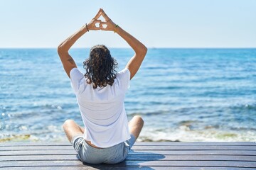 Fototapeta na wymiar Young hispanic man doing yoga exercise sitting on bench at seaside