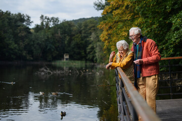 Happy senior couple at autumn walk near the lake, having break.