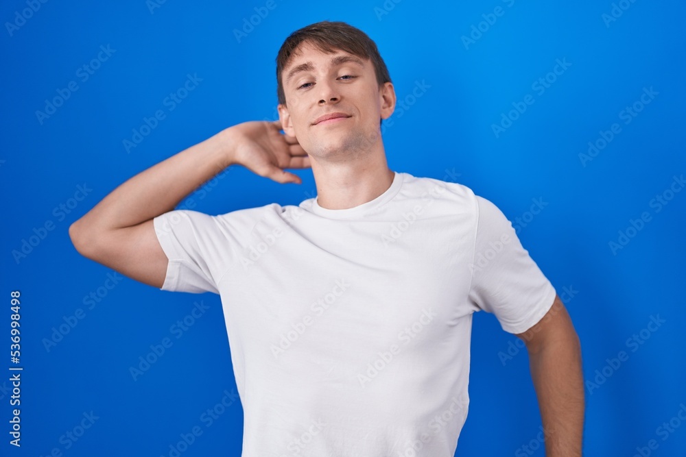 Sticker Caucasian blond man standing over blue background stretching back, tired and relaxed, sleepy and yawning for early morning