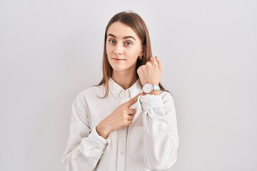 Young caucasian woman standing over isolated background in hurry pointing to watch time, impatience, looking at the camera with relaxed expression