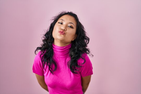 Young asian woman standing over pink background looking at the camera blowing a kiss on air being lovely and sexy. love expression.