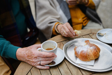 Close-up of senior couple enjoying cup of coffee and cake outdoor in cafe.